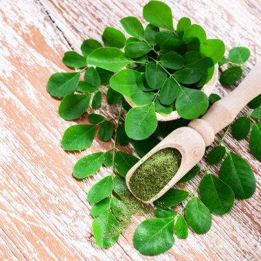 Moringa tozu (Moringa Oleifera) ve ahşap arka planda taze Moringa yaprakları. Sağlıklı ürün, süper yiyecek, vitamin. Kare atış.