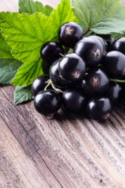 Köhne eski ahşap arka planda orijinal yapraklı taze, siyah frenk üzümü. Sağlıklı yiyecek, hasat, vitamin.