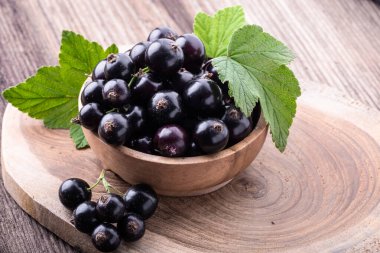 Köy arka planında orijinal yapraklarla ahşap kasede taze, siyah frenk üzümü. Sağlıklı yiyecek, hasat, vitamin.