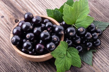 Ahşap kasede taze, siyah frenk üzümü. Köhne arka planda orijinal yapraklar, yakın plan görüntüsü. Sağlıklı yiyecek, hasat, vitamin.