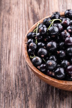 Ahşap arka planda taze siyah üzümlü ahşap kasenin yarısı. Sağlıklı gıda, hasat, vitamin, detoks, vegan, vejetaryen, alternatif tıp.