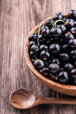 Büyük ahşap kasenin yarısı taze siyah frenk üzümü ve ahşap arka planda yakın plan manzaralı kaşık. Sağlıklı gıda, hasat, vitamin, detoks, vegan, vejetaryen, alternatif tıp.