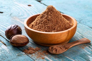 Tüm kabuklu ceviz, çatlak ve hindistan cevizi tozu ahşap bir kâse ve kaşık içinde eski mavi kırsal arka planda yakın plan. Hint baharatı.