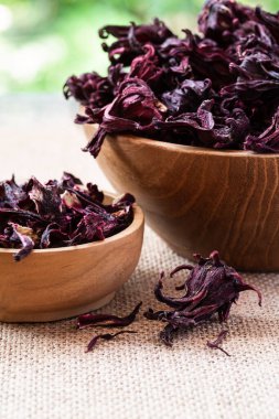 Hibiscus (Roselle, karkade) ahşap kaplamalı kuru çiçekler, çuval bezi üzerinde yeşil doğal arka plan ve fotokopi alanı yakın plan. Sağlıklı organik bitki çayı..