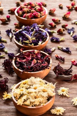 Köy arka planında, ahşap kaselerde çay çeşitleri. Çeşitli bitkisel sağlıklı çay türleri gül, amber çiçeği, kelebek bezelyesi, kasımpatı..