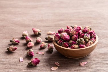 Ahşap kasede pembe kırmızı kurumuş gül tomurcukları ve eski ahşap arka plan kopyasının yaprakları. Sağlıklı egzotik Asya organik çayı.