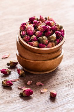 Ahşap kaselerde pembe kırmızı kurumuş gül tomurcukları ve eski ahşap arka plan kopyasının yaprakları. Sağlıklı egzotik Asya organik çayı.