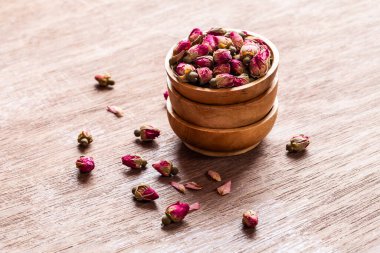 Ahşap kaselerde pembe kırmızı kurumuş gül tomurcukları ve eski ahşap arka plan kopyasının yaprakları. Sağlıklı egzotik Asya organik çayı.