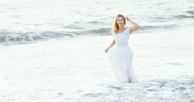 Çekici, mutlu, olgun, sarışın, uzun beyaz elbiseli, Asya 'nın tropikal kumsalında, su kenarında neşeli gülümseyen sarışın kadın. Romantik seyahat tatili, aktif yaşam tarzı, bağımsız ve kendine güveni olan biri..