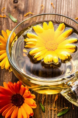 Ahşap arka planda kurumuş çiçeklerle şeffaf cam bardakta bitkisel çay. Sağlıklı çiçek çayı, alternatif tıp.