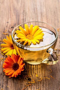 Ahşap arka planda kurumuş çiçeklerle şeffaf cam bardakta bitkisel çay. Sağlıklı çiçek çayı, alternatif tıp.
