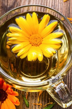 Ahşap arka planda kurumuş çiçeklerle şeffaf cam bardakta bitkisel çay. Sağlıklı çiçek çayı, alternatif tıp.