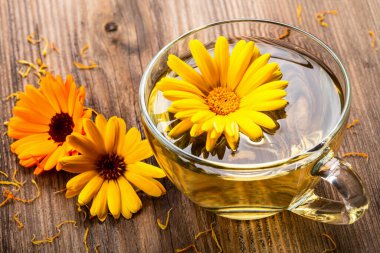 Ahşap arka planda kurumuş çiçeklerle şeffaf cam bardakta bitkisel çay. Sağlıklı çiçek çayı, alternatif tıp.