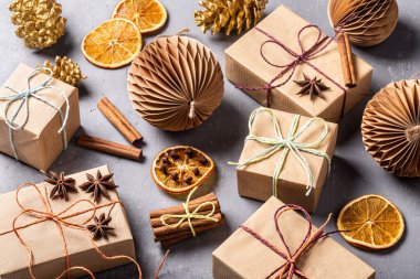 Kraft kağıdından hediyeler ve gri beton arka planda çevre dostu dekorasyonlarla yapılmış şenlikli bir Noel kompozisyonu. Noel israfı.
