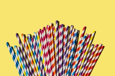 Çok renkli kamış kağıt tüpleri. Kopyalama alanı olan parlak sarı pastel arka planda parti için plastik yok. Üst manzara, düz uzanma.