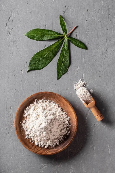 キャッサバ マニオック の小麦粉を木製のボウルに入れ 灰色の背景の上面に元の葉を付けます 代替グルテンフリー小麦粉 健康食品 — ストック写真