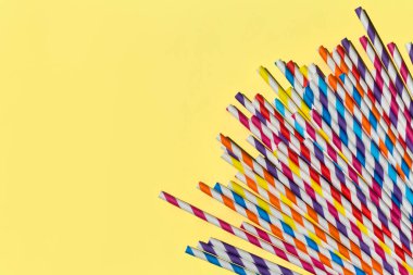 Çok renkli kamış kağıt tüpleri. Kopyalama alanı olan parlak sarı pastel arka planda parti için plastik yok. Üst manzara, düz uzanma.