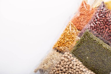 Beyaz arka planda vejetaryen gıda malzemeleri var. Renkli çeşitli mısır gevrekleri ve plastik ambalajlı baklagiller. Protein ürünleri. Yiyecek teslimatı, bağış, koronavirüs karantinası..