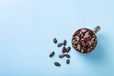 Kahverengi seramik bardakta tüm kakao çekirdekleri mavi üst görünümde sol tarafta. Gıda arkaplanı. 