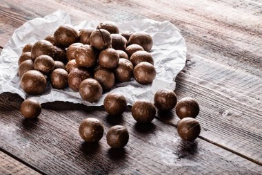 Organik olgun Macadamia fındıkları eski ahşap masa üzerinde beyaz kağıt üzerinde. Sağlıklı vejetaryen yemeği, vitamin....