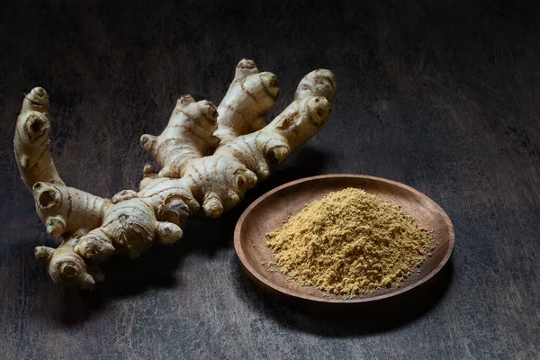 Fresh organic ginger root and powder in wooden bowl on dark old rustic background with copyspace. Healthy food, diet, alternative medicine, Ayurvedic.