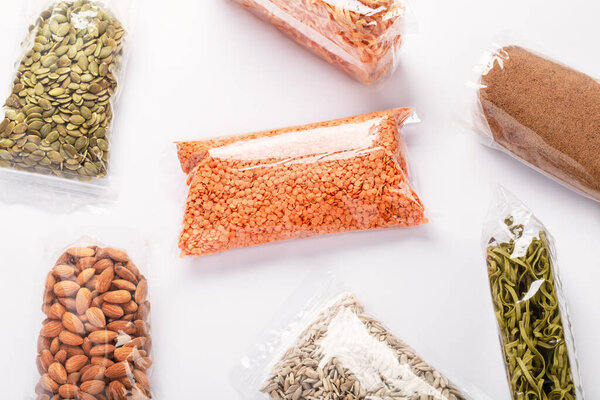 Vegan food supplies on white background with copyspace. Group of colorful various cereals, seeds, nuts and legumes in plastic wrap. Healthy protein products. Food delivery, donation, coronavirus quarantine.