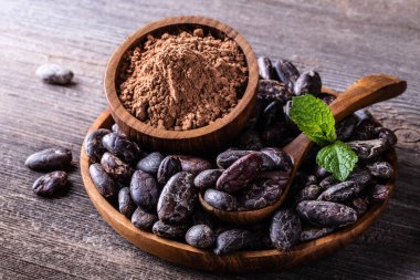 Kakao çekirdekleri ve toz, tahta kâse kaşığında, eski kırsal arka planda, yakın plan seçici odak noktasında..