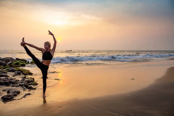Middle age woman in black doing yoga on sand beach in India  standing asana sunset time.