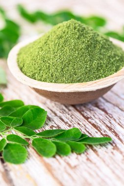 Moringa tozu (Moringa Oleifera) hindistan cevizi kasesinde, ahşap arka planda orijinal taze Moringa yapraklarıyla. Sağlıklı ürün, süper yiyecek, vitamin.