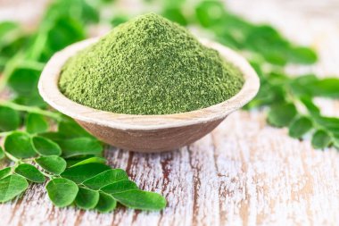 Moringa tozu (Moringa Oleifera) hindistan cevizi kasesinde, ahşap arka planda orijinal taze Moringa yapraklarıyla. Sağlıklı ürün, süper yiyecek, vitamin.