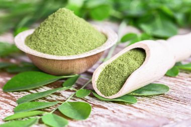 Moringa tozu (Moringa Oleifera) hindistan cevizi kasesinde, ahşap arka planda orijinal taze Moringa yapraklarıyla. Sağlıklı ürün, süper yiyecek, vitamin.