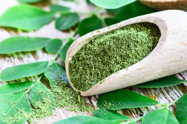 Ahşap kepçe içinde Moringa tozu ve ahşap masa üzerinde orijinal taze Moringa yaprakları. Makro atış.