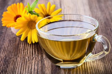 Calendula (Marigold), ahşap arka planda şeffaf cam bardakta bitki çayı.