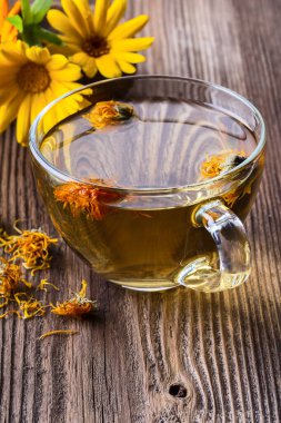 Ahşap zemin üzerinde şeffaf cam bir fincanda bitkisel çay ve dikey fotokopi.