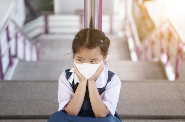 Başbakan 2.5. Toz veya COVID-19 virüsünü korumak için beyaz maskeli Asyalı çocuk ya da çocuk öğrenci ya da çocuk maskesi takıyor ve ne yazık ki okula döndüğü için sıkılmak üzere gökyüzü tren istasyonunda ya da üst geçitte parmaklıklara yaslanıyor.