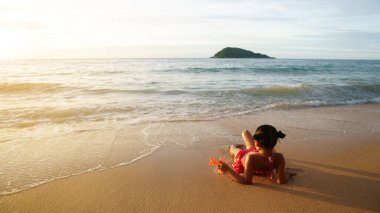 Mutlu Asyalı çocuk ya da küçük kız kumsalda ya da mavi denizde uzanır sabah güneşinde ya da gün batımında altın sıcacık güneş ışığıyla yaz tatilinde dinlenir ve bikini giyer.