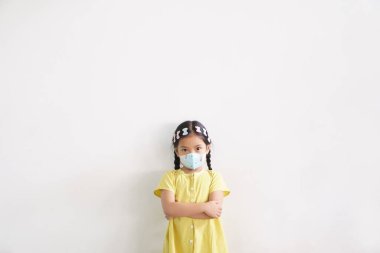 Asyalı çocuk kollarını kavuşturmuş ya da çocuk N95 beyaz yüz maskesi takmış, ağzı kapalı, grip olmuş, öksürük hastası ve duvarda 2,5 toz veya Coronavirus covid-19 'u koruyor.