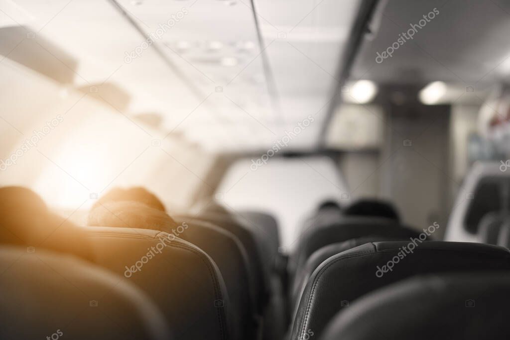 interior of airplane or aircraft with passengers or tourist and back people head on black seats or chair in eco class and flying for transportation or holiday travel and tourism from airport with sun