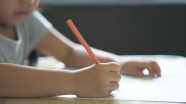 Çocukların eli ya da kız çocuğu gülümseme turuncu boyama ya da boya eğitimi öğrenme ve beyaz kağıt üzerinde öğretmenle ödev yapma ve anaokulunda ya da 4K masasındaki anaokulunda mutlu olma.