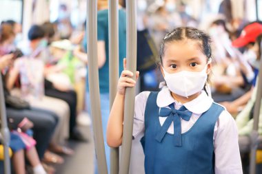 Gökyüzü treninde ve metroda Coronavirus 'u korumak için maske takan Asyalı bir çocuk ya da çocuk öğrenci ya da kız öğrenci okul taşımacılığına dönmek için sokak kentinde direği ya da demiryolunu tutmak için metro ya da birçok insanı korumak için.