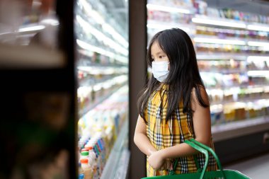 Kapalı ağız için beyaz yüz maskesi takan Asyalı çocuk ya da çocuk Coronavirus covid-19 'u korumak için grip ve grip öksürüğü ya da süpermarkette ya da markette süt almak için sepet tutan toz.