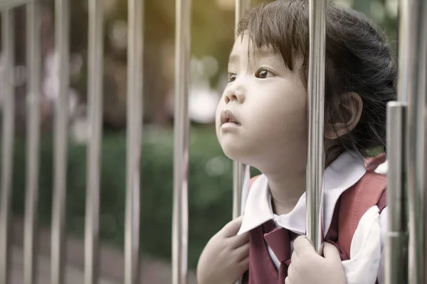 homesick asian child or kid girl student sadly face or lonely unhappy with miss something and holding fence from go to school or back to school for study preschool at kindergarten education on 3 years