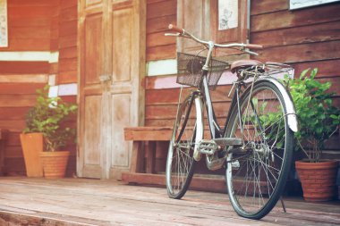 Eski moda siyah ve kahverengi bisiklet ya da motorsiklet retro ahşap ev terası önünde ahşap kapılı ve pencereli iç mimari dekoru için saksıdaki ağaç ya da güneş ışığıyla geçmiş bellek arka planı