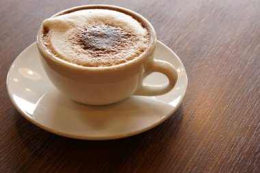 Sabah kahvaltı için ahşap masanın üzerinde beyaz bardakta sıcak kapuçino kahvesi işe gitmeden önce sıcak beyaz ve kafede ya da uzay boşluğu olan bir ofiste doğa ışığı.