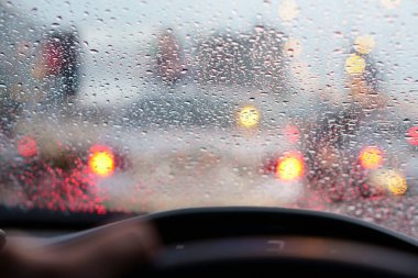 İnsanlar araba aynasında ya da ön camında araba ve su damlacıkları kullanıyor. Otobanda yağmur ve trafik sıkışıklığı var. Arabanın arkasında kırmızı ışık var.