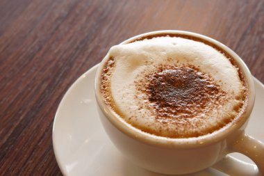 Sabah kahvaltı için ahşap masanın üzerinde beyaz bardakta sıcak kapuçino kahvesi işe gitmeden önce sıcak beyaz ve kafede ya da uzay boşluğu olan bir ofiste doğa ışığı.