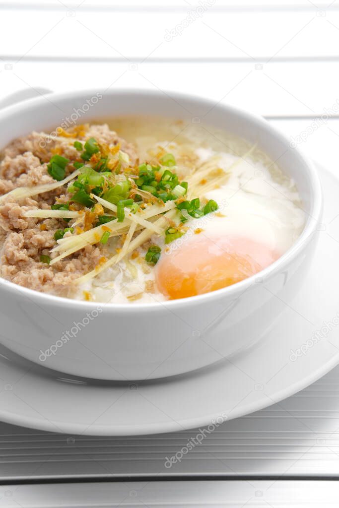 vertical pork chops rice porridge or congee with soft boiled egg and vegetable in the white bowl with spoon on the aluminium table for delicious breakfast and clean food in the morning