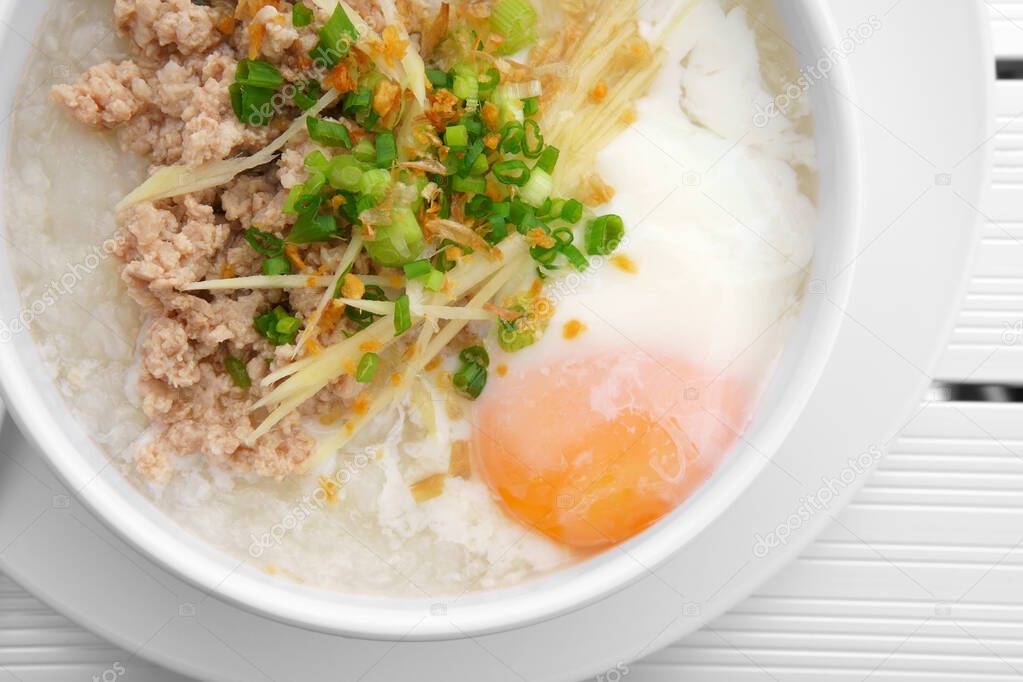 pork chops rice porridge or congee with soft boiled egg and vegetable in the white bowl with spoon on the top view aluminium and white table for delicious breakfast and clean food in the morning