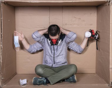  Karton ofiste oturan genç bir işçi yüzüne maske takıyor ve maskelerin türünü gösteriyor.