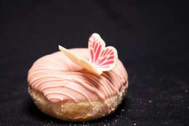 Pembe çikolatayla kaplanmış ve güzel bir kelebekle süslenmiş güzel bir çörek.